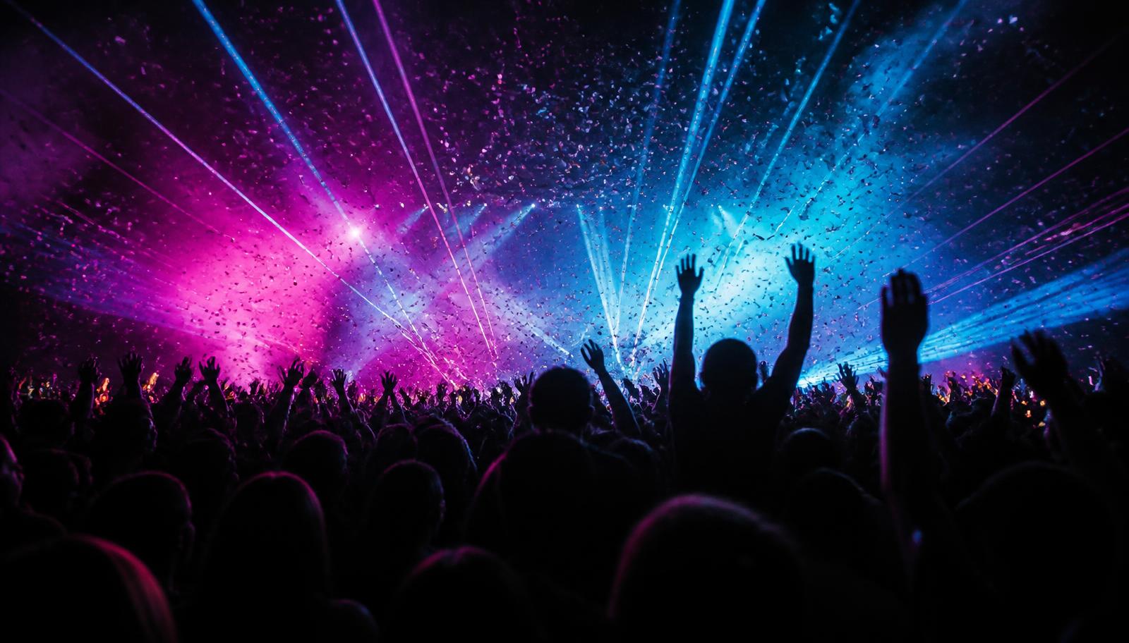 Crowd with hands raised under magenta and cyan lasers at a Beatverse show
